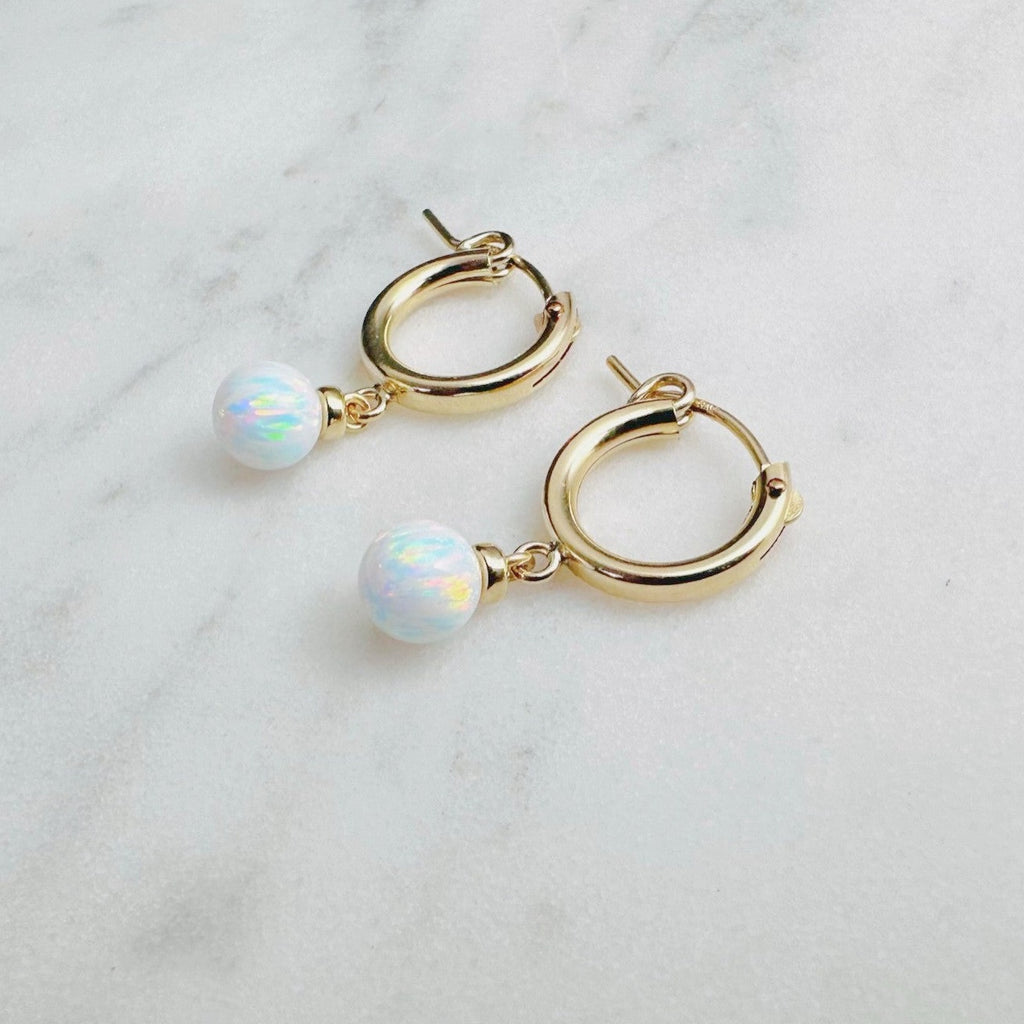 "Dainty gold huggie hoop earrings with white opal gemstones on marble background – minimalist everyday jewelry for women"