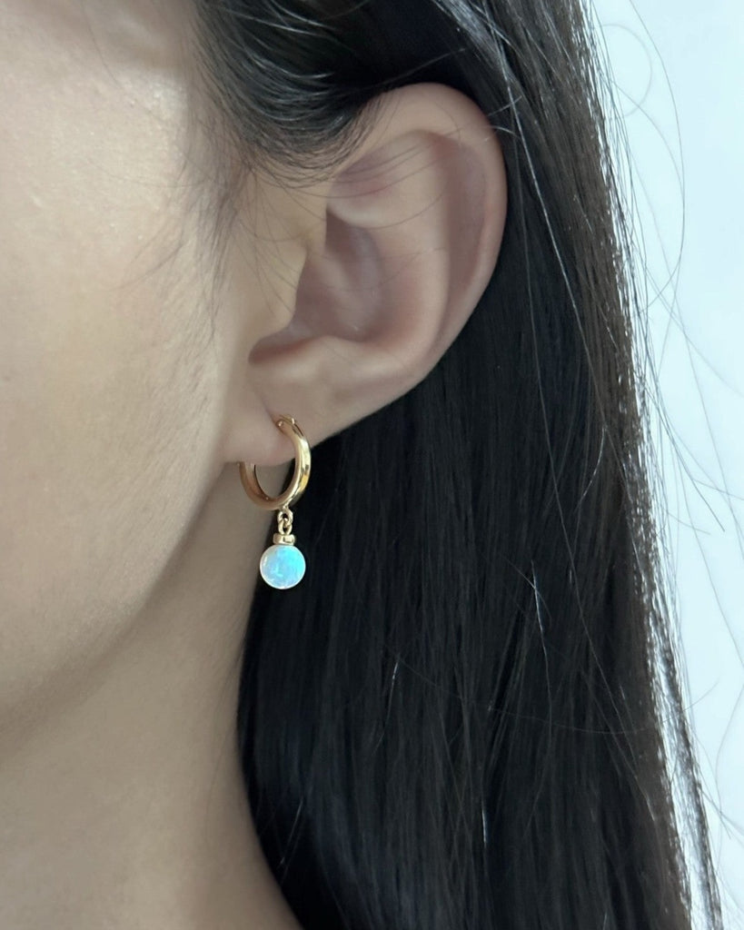 "Petite white opal huggie earrings worn on ear – delicate gold hoops with iridescent opals for layered looks"
