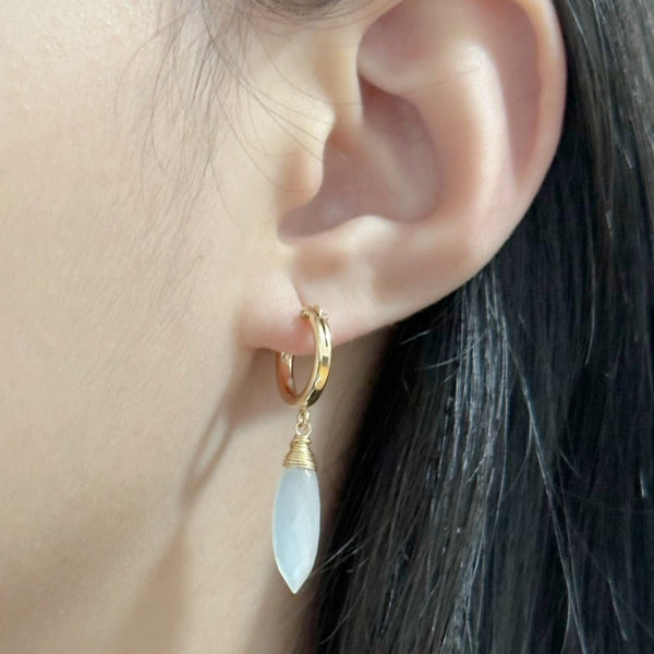 Petite white moonstone huggie earrings worn on ear – glowing white adularescence in gold hoops